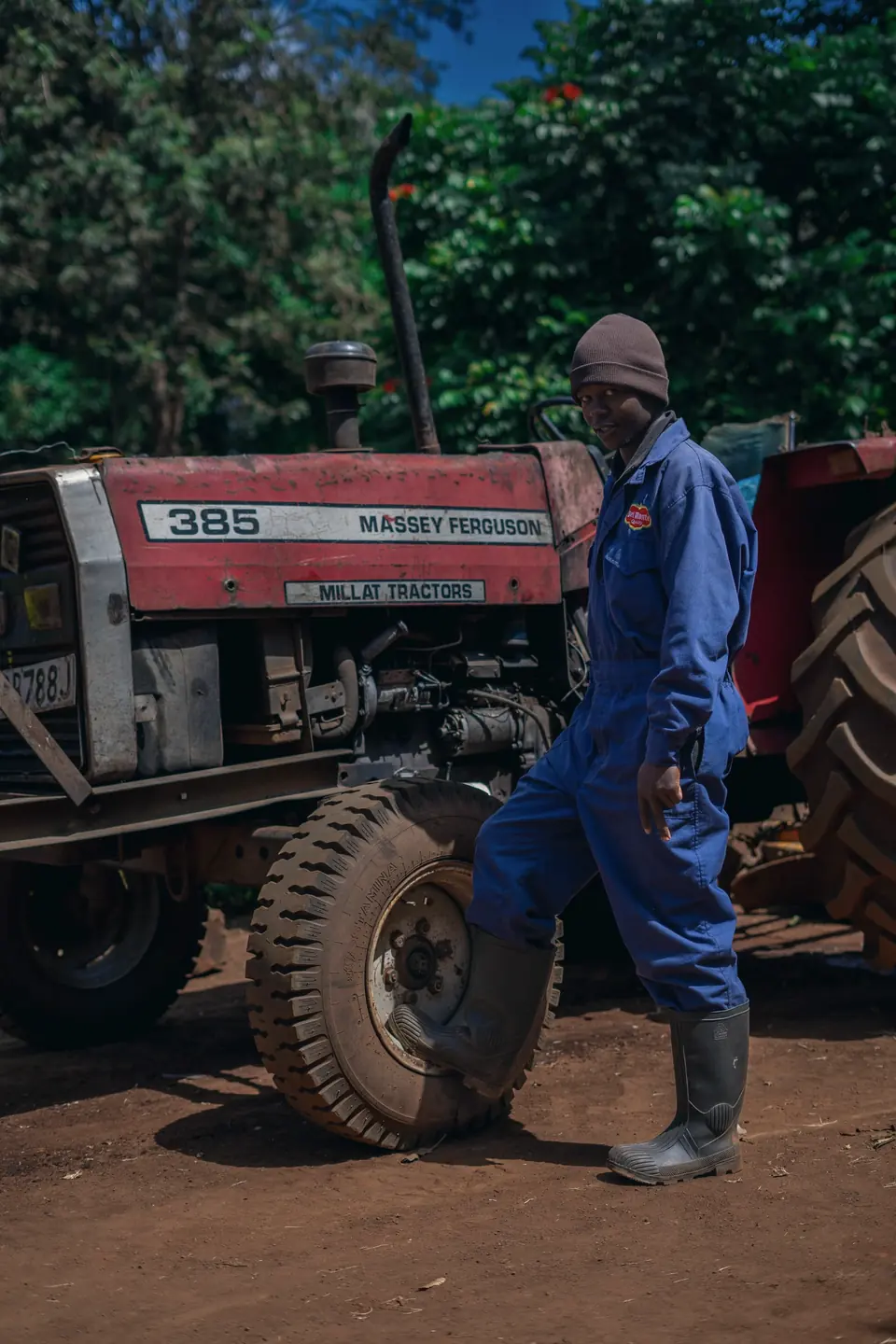 A farm worker in blue overalls stands beside a red Massey Ferguson tractor.